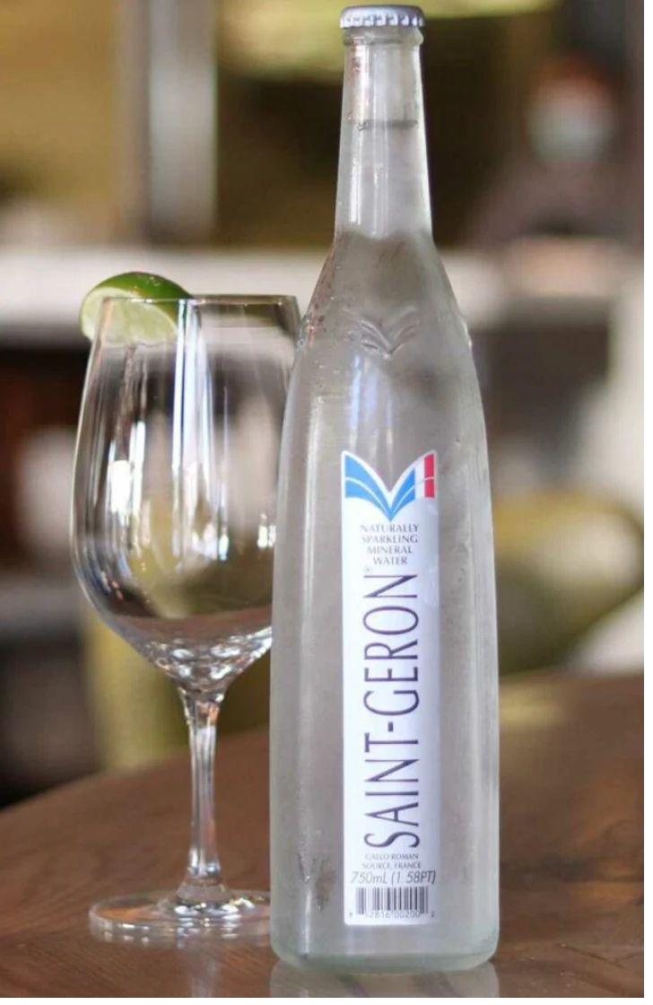 Saint-Géron bottle beside a wine glass garnished with lime at a restaurant table